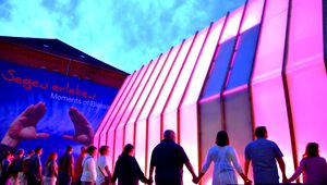 bunt von innen erleuchtete Kirche, um die eine Menschenkette steht